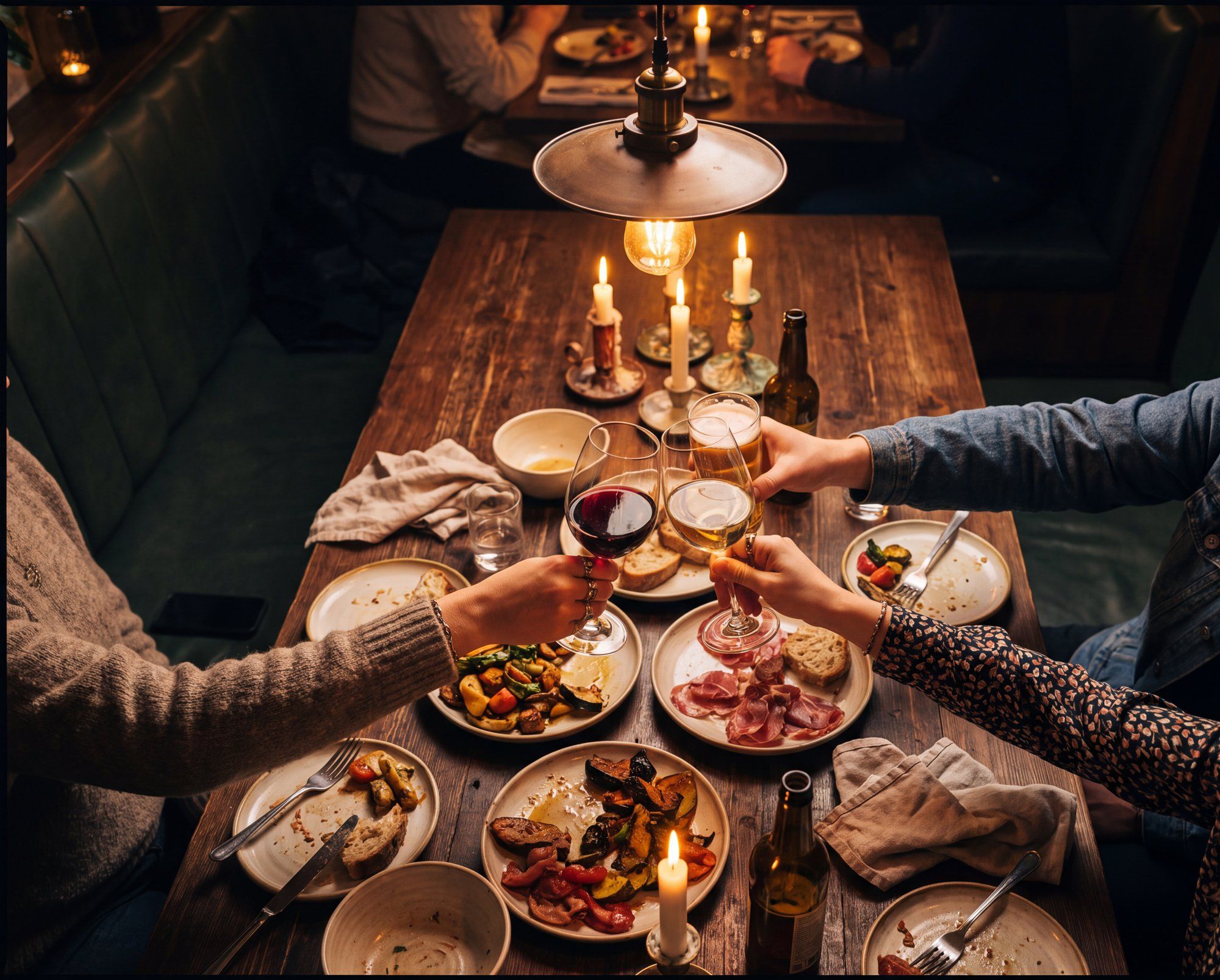 Regulars raising glasses over shared plates at a candlelit table, seen from above.